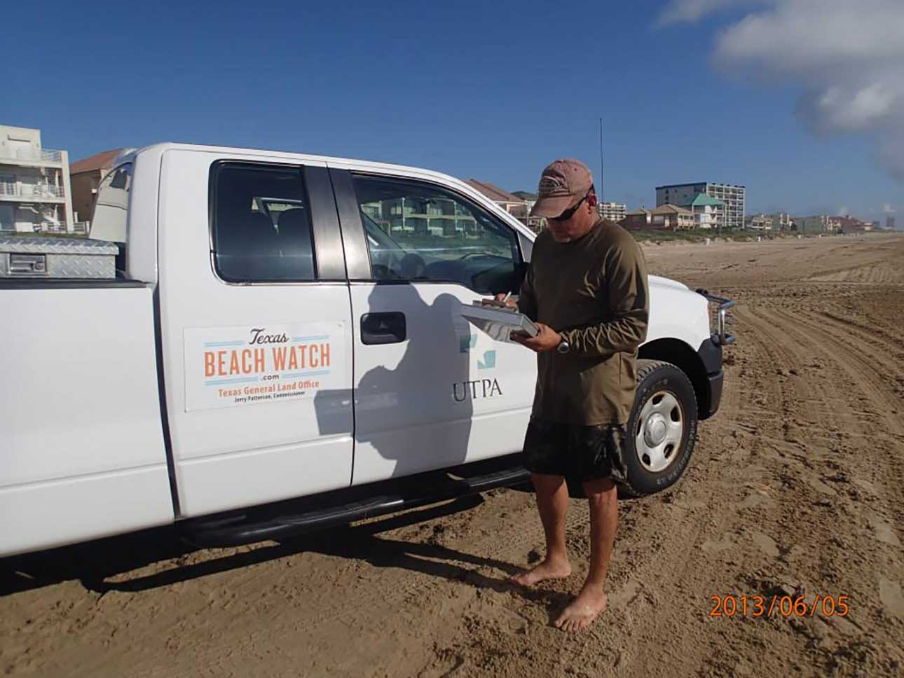 A man standing next to a pick up truck on the beach filling some papers