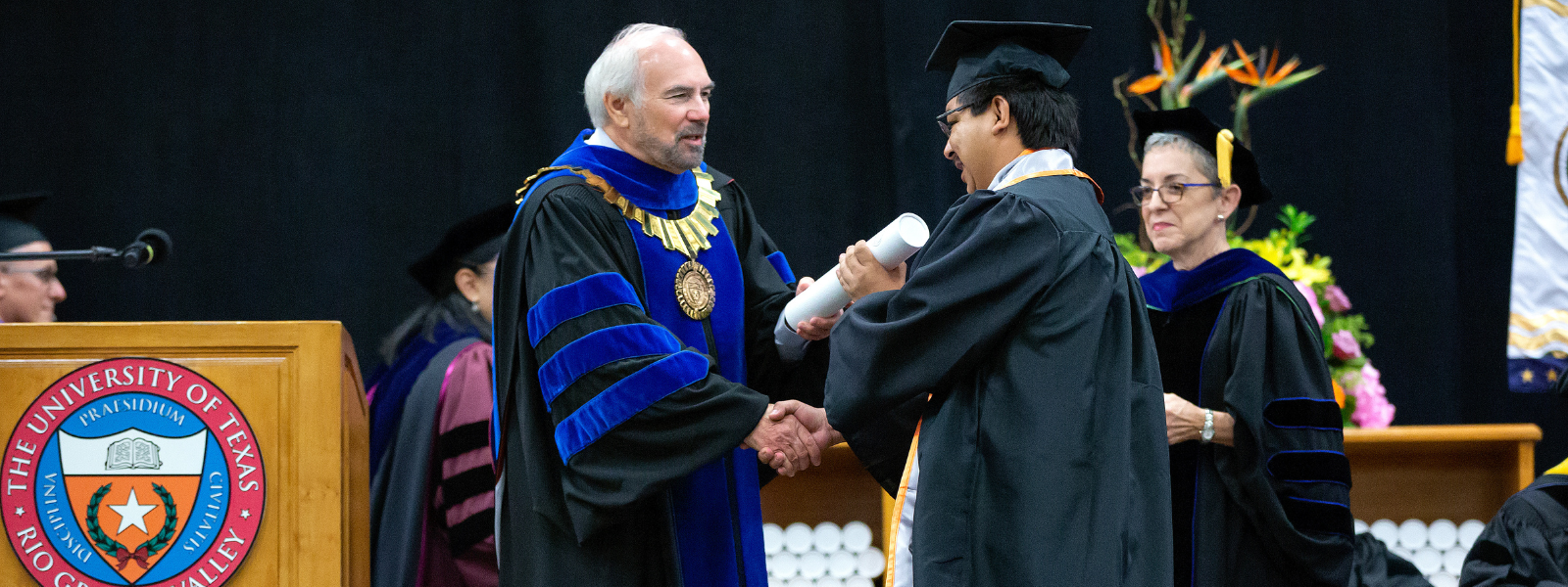President Bailey presents a white diploma case to a student during the graduation commencement ceremony.
