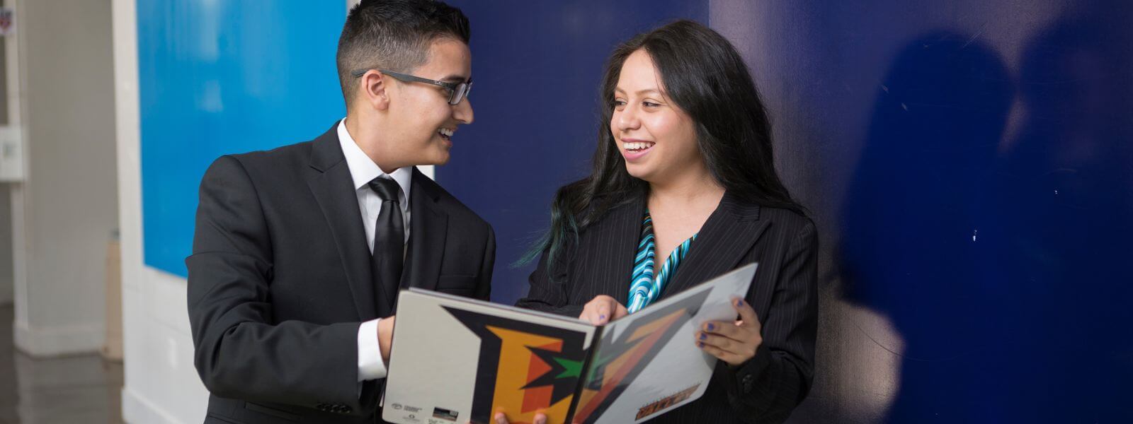 Two students in professional attire smiling at each other