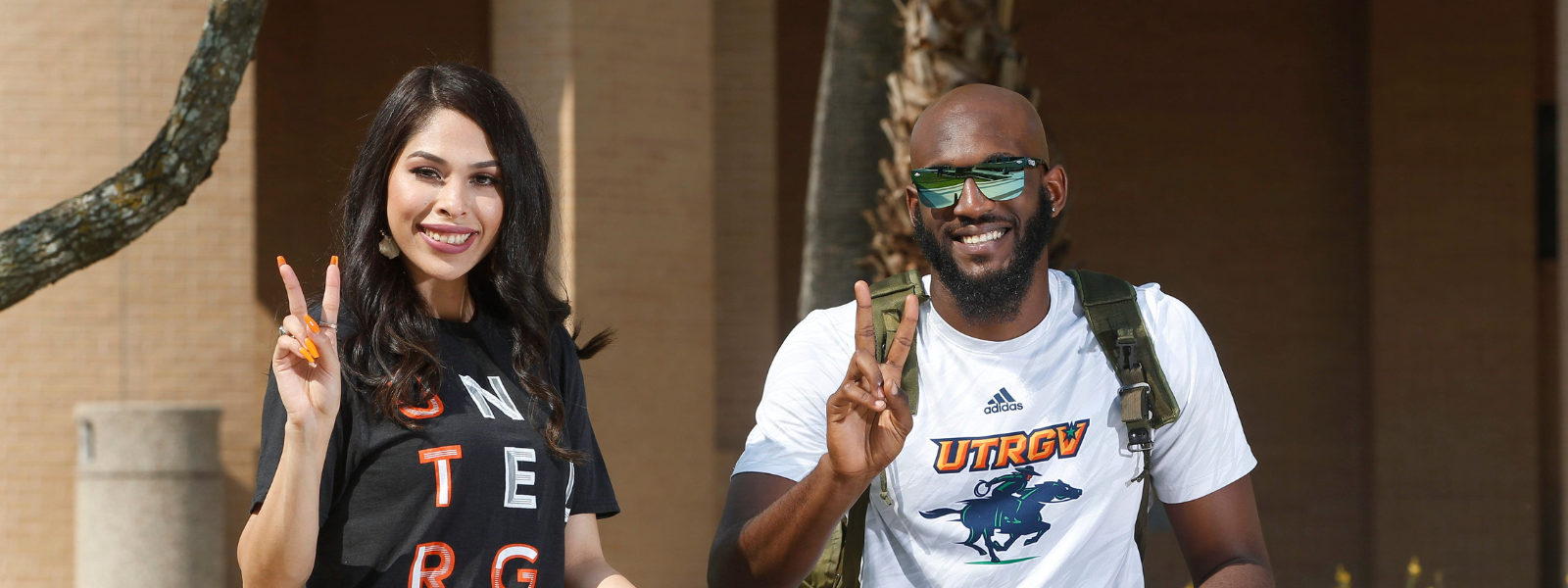 Students sitting outdoors while giving a V's up (victory hand sign.)