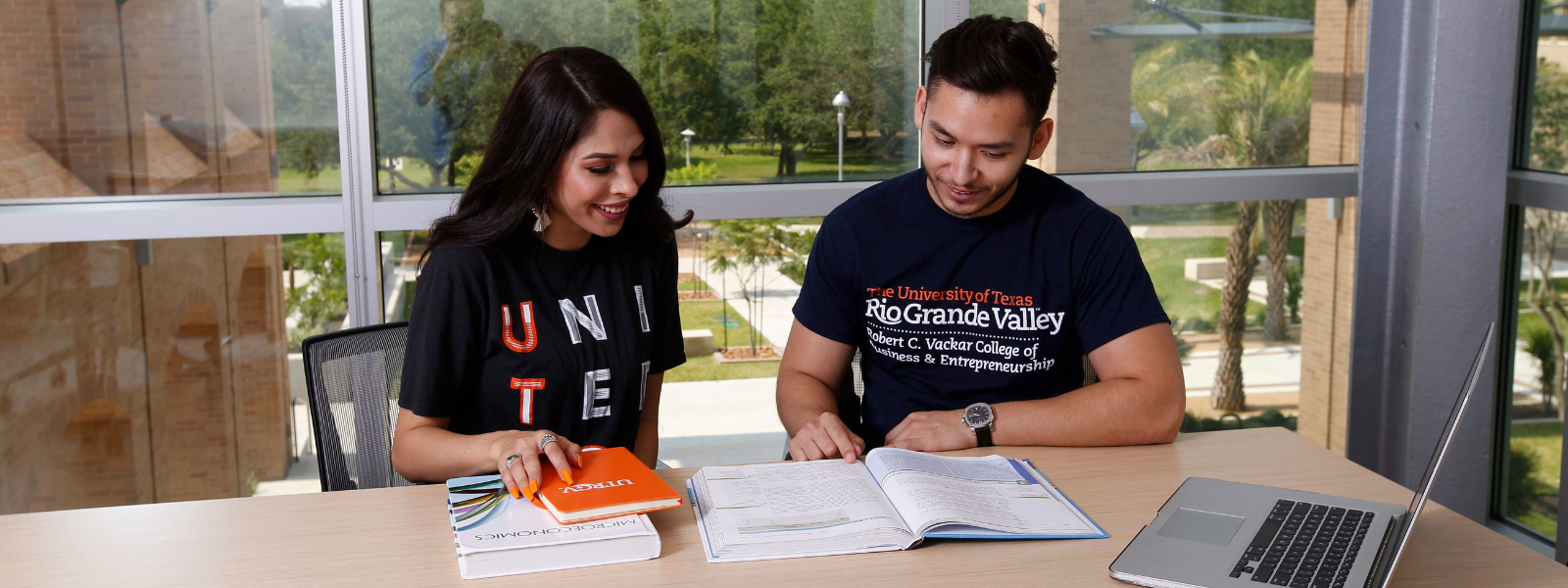 Two students studying at a desk with opened books in front of them.