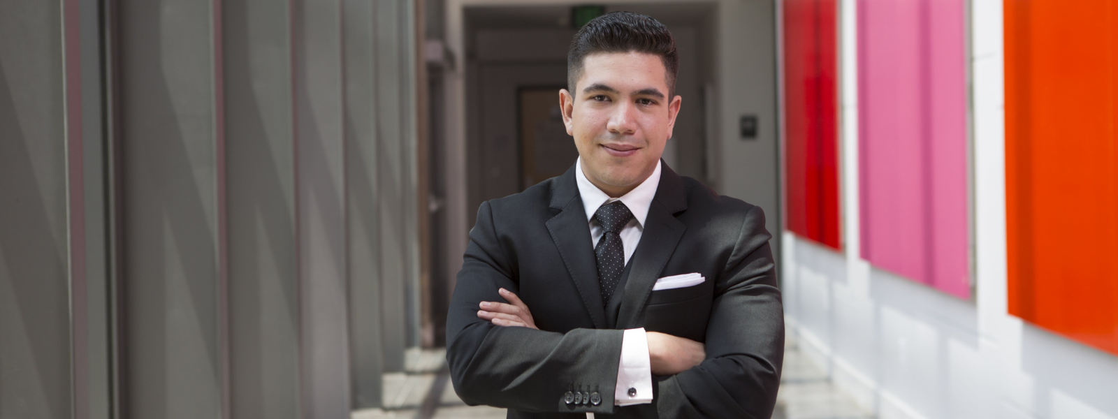 Smiling student in a business suit, confidently posing with arms crossed.