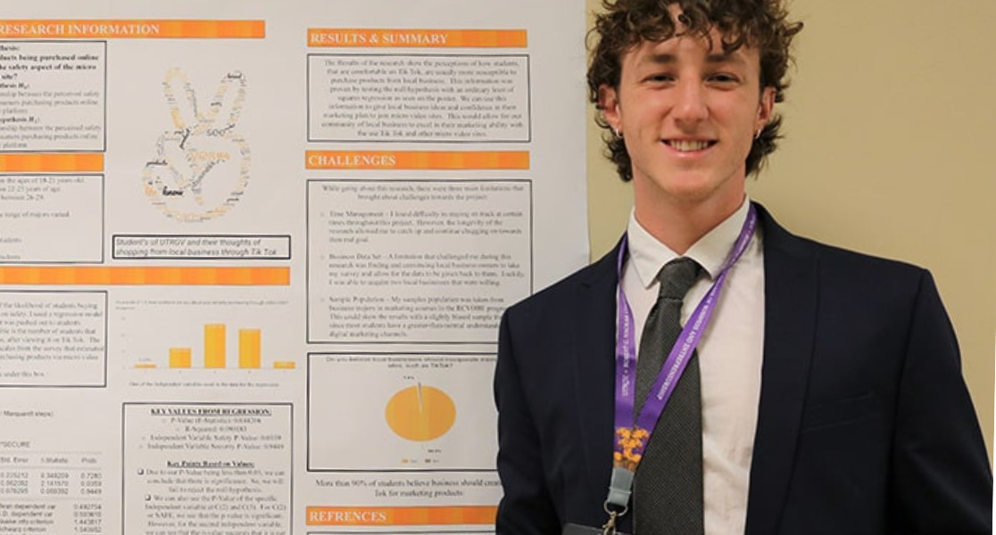 Student standing behind his presentation poster while smiling and holding a certificate. 