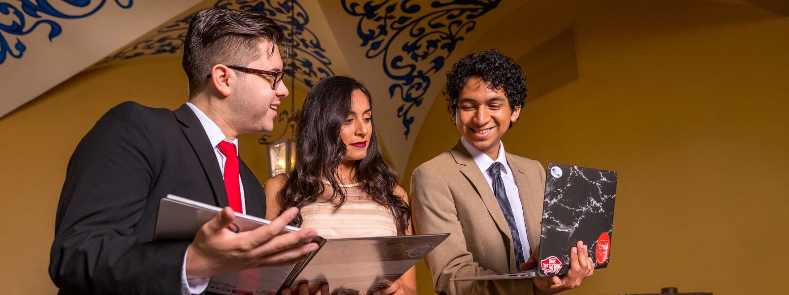 Students smile while holding documents and laptop